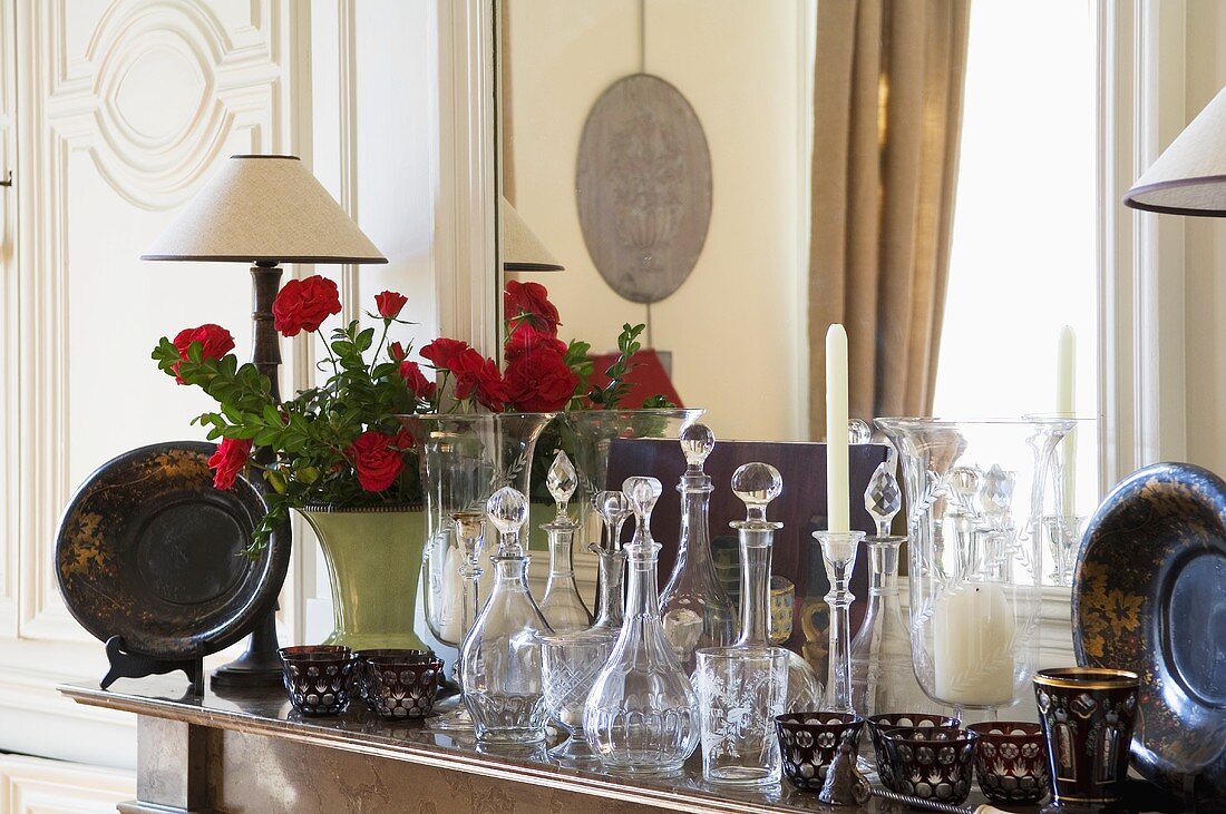 A collection of antique glass bottles and metal bowls in front of a mirror on a mantelpiece
