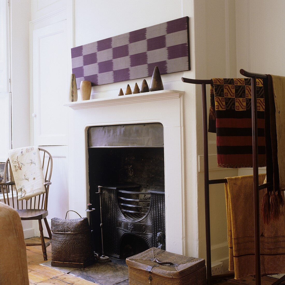 A white fireplace with cladding and a metal stand hung with ethnic cloths