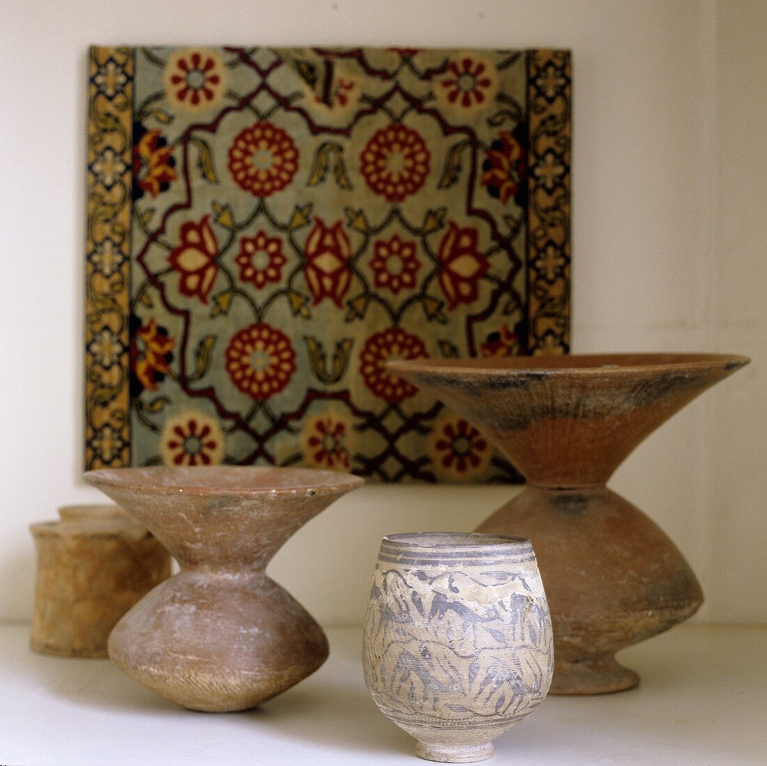 Antique folk art style stone containers in front of a picture with an oriental design