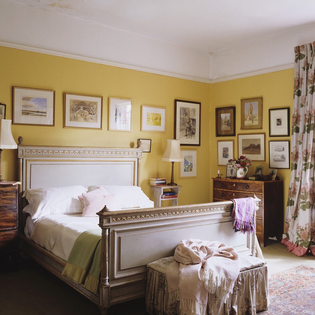 A bedroom in a country house with a white antique wooden bed and pictures hanging on a yellow wall