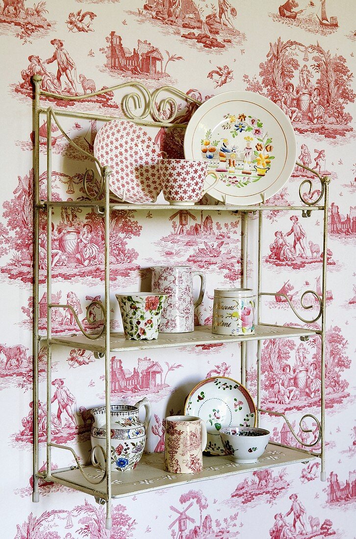 Crockery on an antique metal shelf on a wall papered with country images