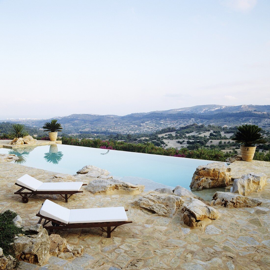 Loungers on a natural stone floor by a pool with a view of the Spanish landscape