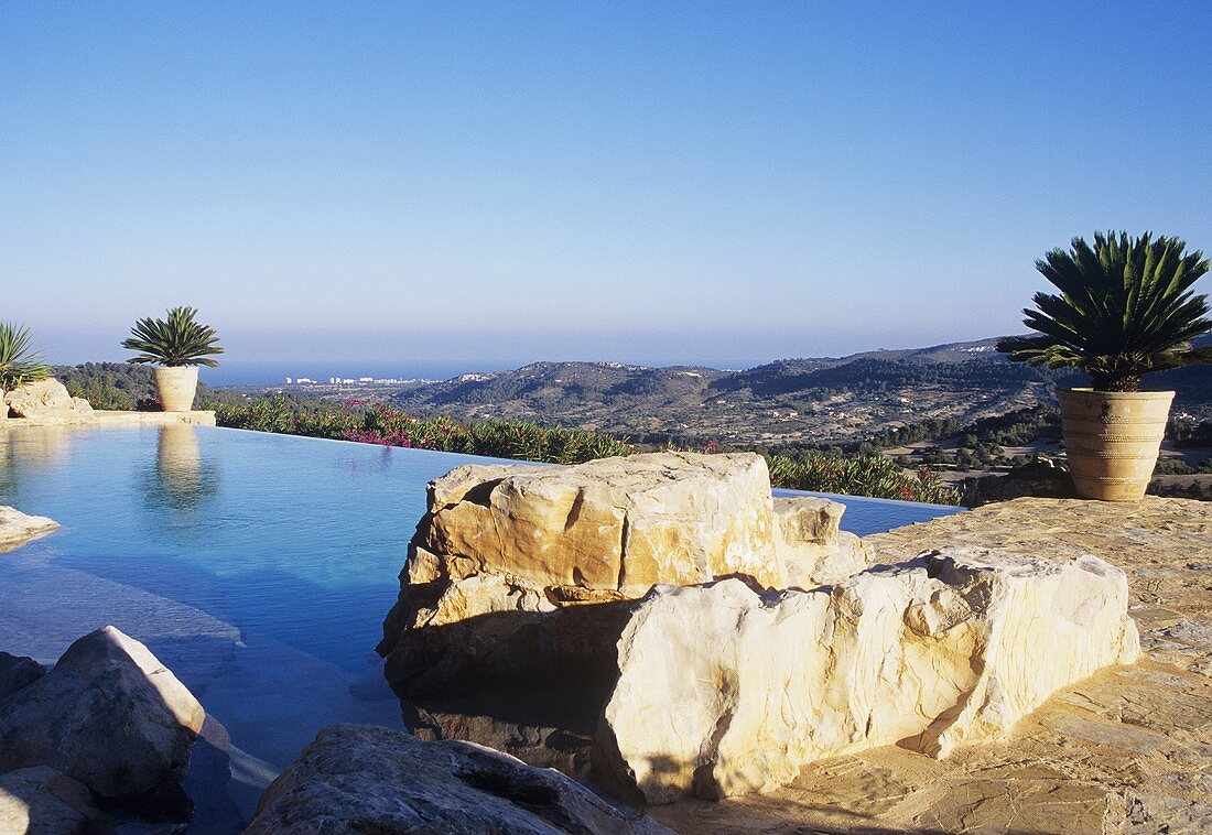 Felsblöcke und Pflanzenkübel am Pool mit Ausblick auf die spanische Landschaft
