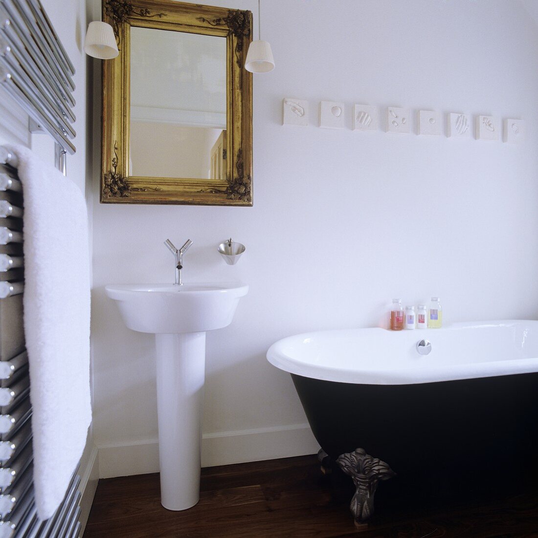 A designer wash basin and a mirror with a gold frame and an antique bathtub with feet in a bathroom