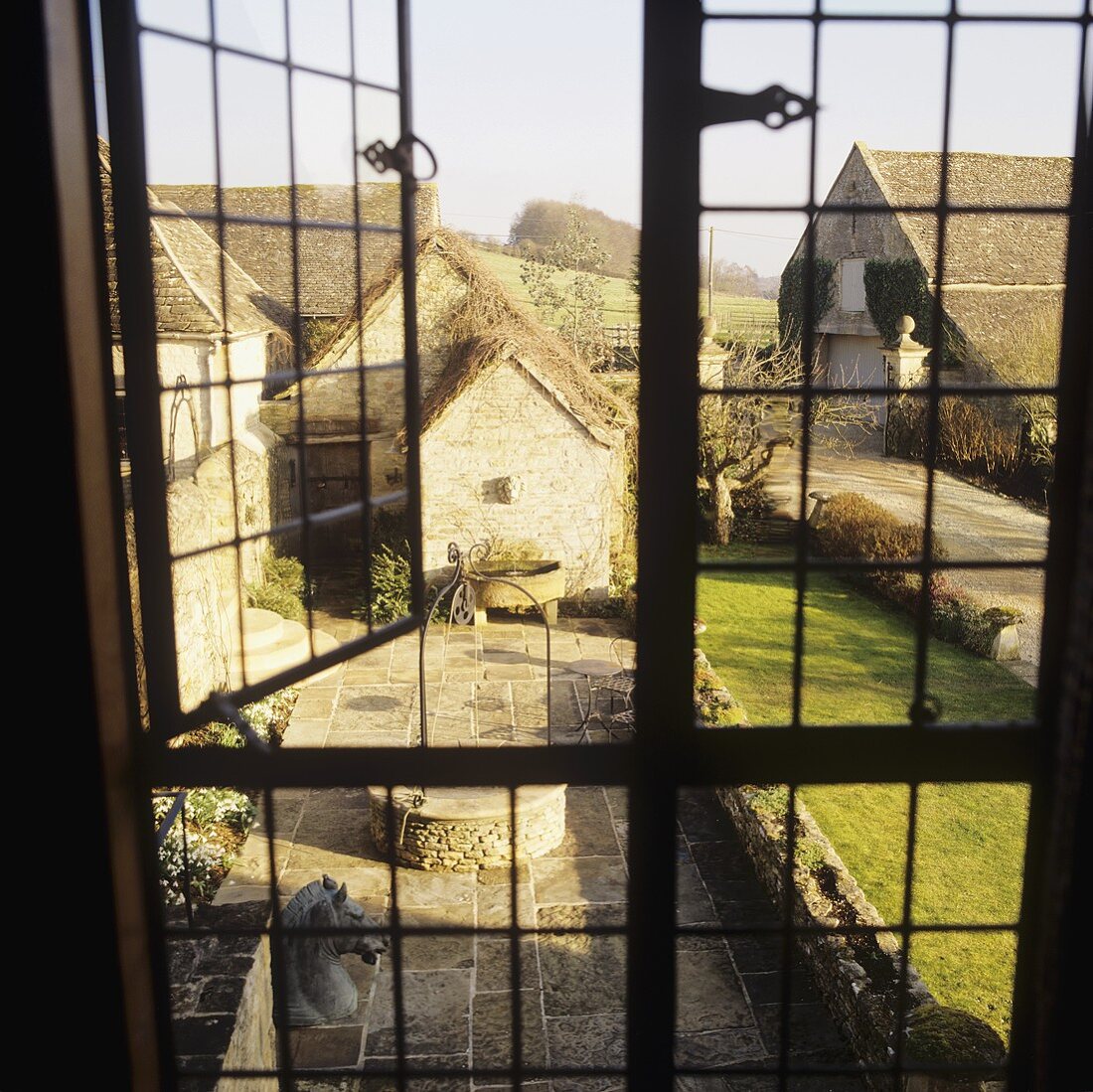 A view through a window onto a courtyard with flagstones and a lawn in front of an English country house