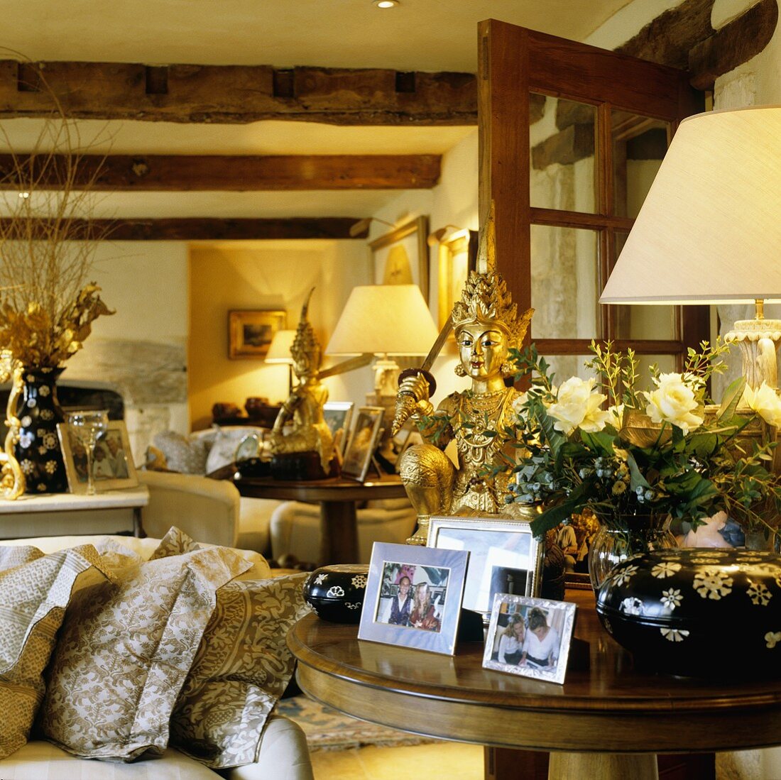 A living room in a country house with a rustic wood beam ceiling and an occasional table with photos and Oriental brass figures