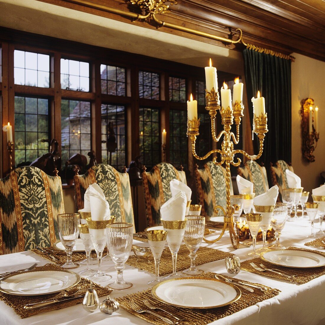 A festively laid table set with silver candle sticks in front of a window in the dining room of a country house
