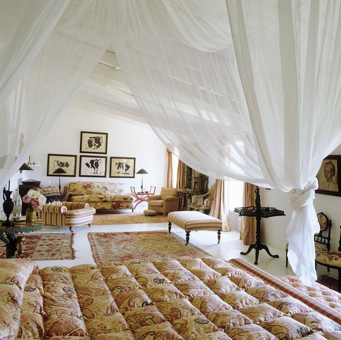 Weisser Stoffhimmel über Bett und elegante Sitzmöbel mit Teppichen im offenen Schlafraum