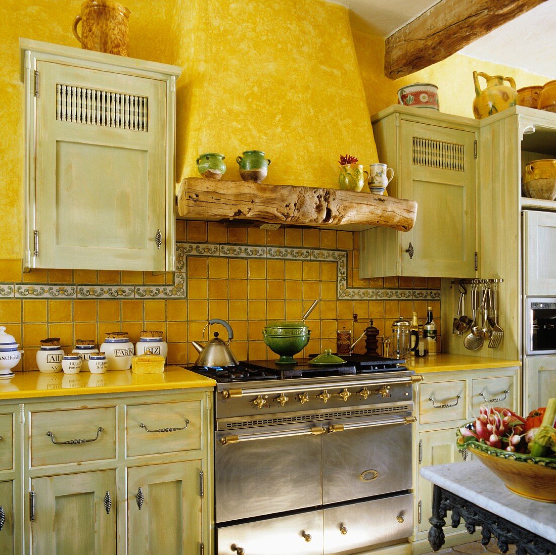 Alte Landhausküche mit kanariengelber Wand und antikem Edelstahlherd mit gemauertem Abzug