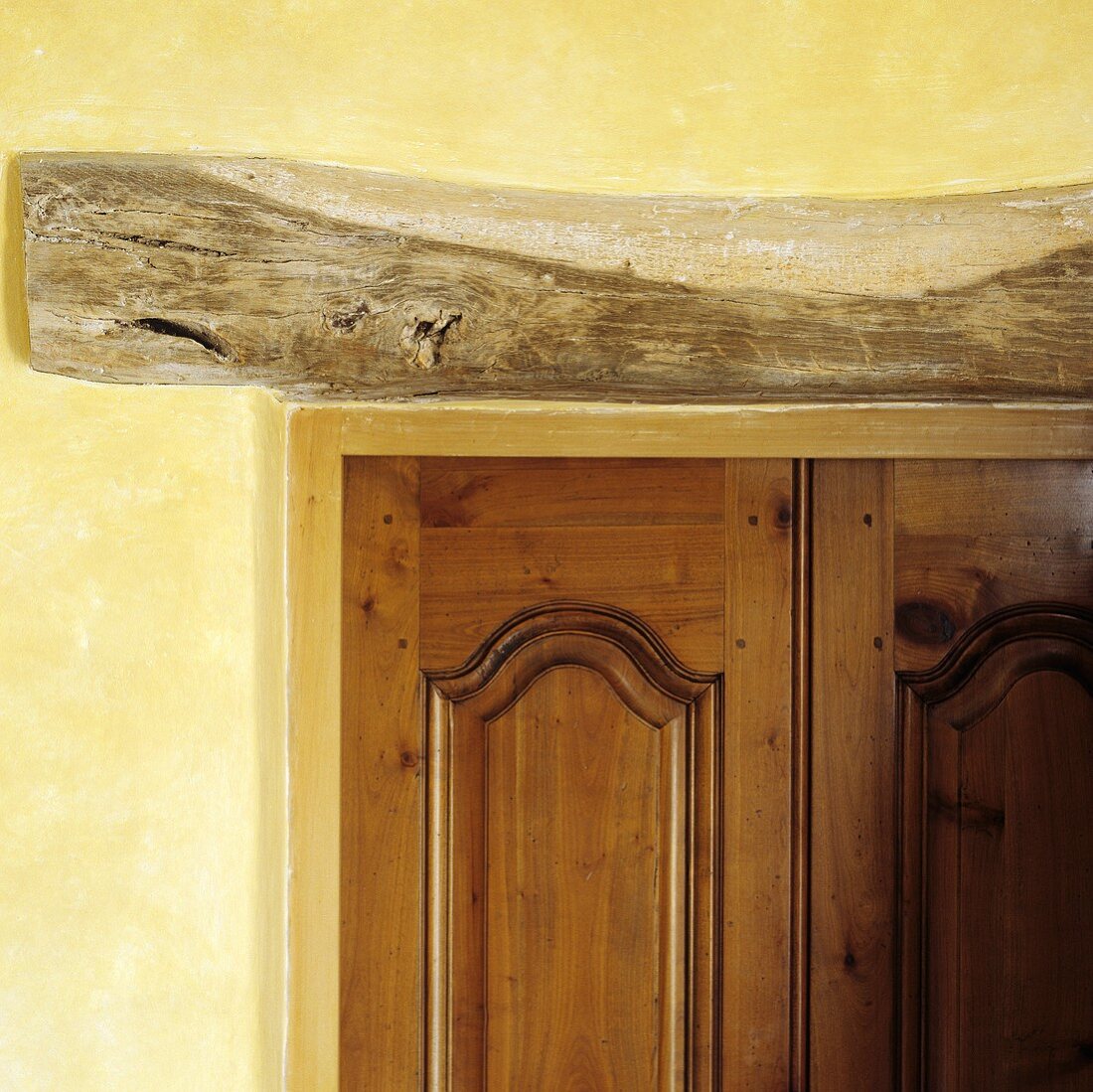 A wooden beam above a door set into a yellow-painted wall