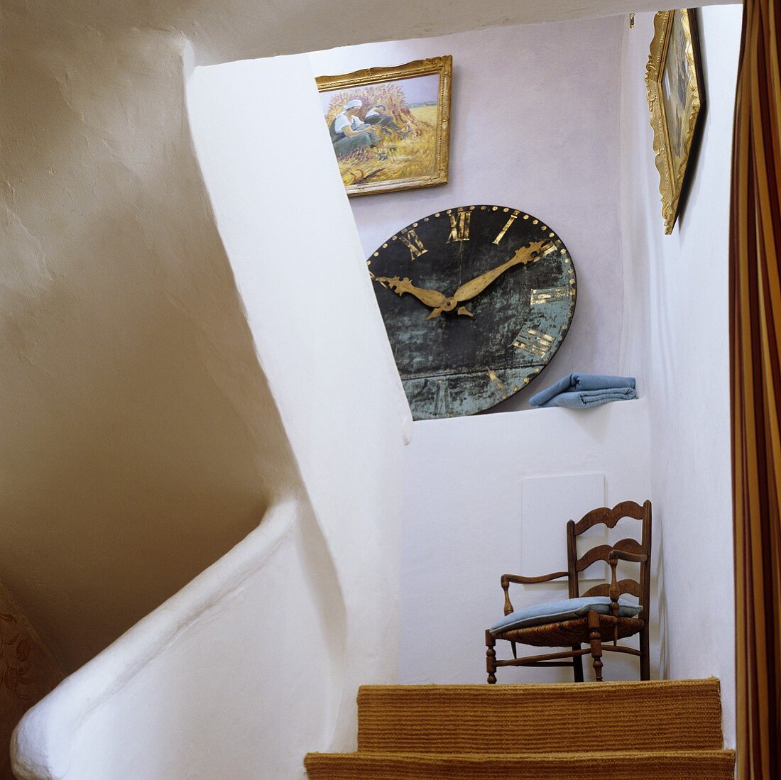 Treppenaufgang mit Blick auf Wanduhr auf der Ablage und Holzstuhl auf dem Podest im ländlichem Treppenhaus
