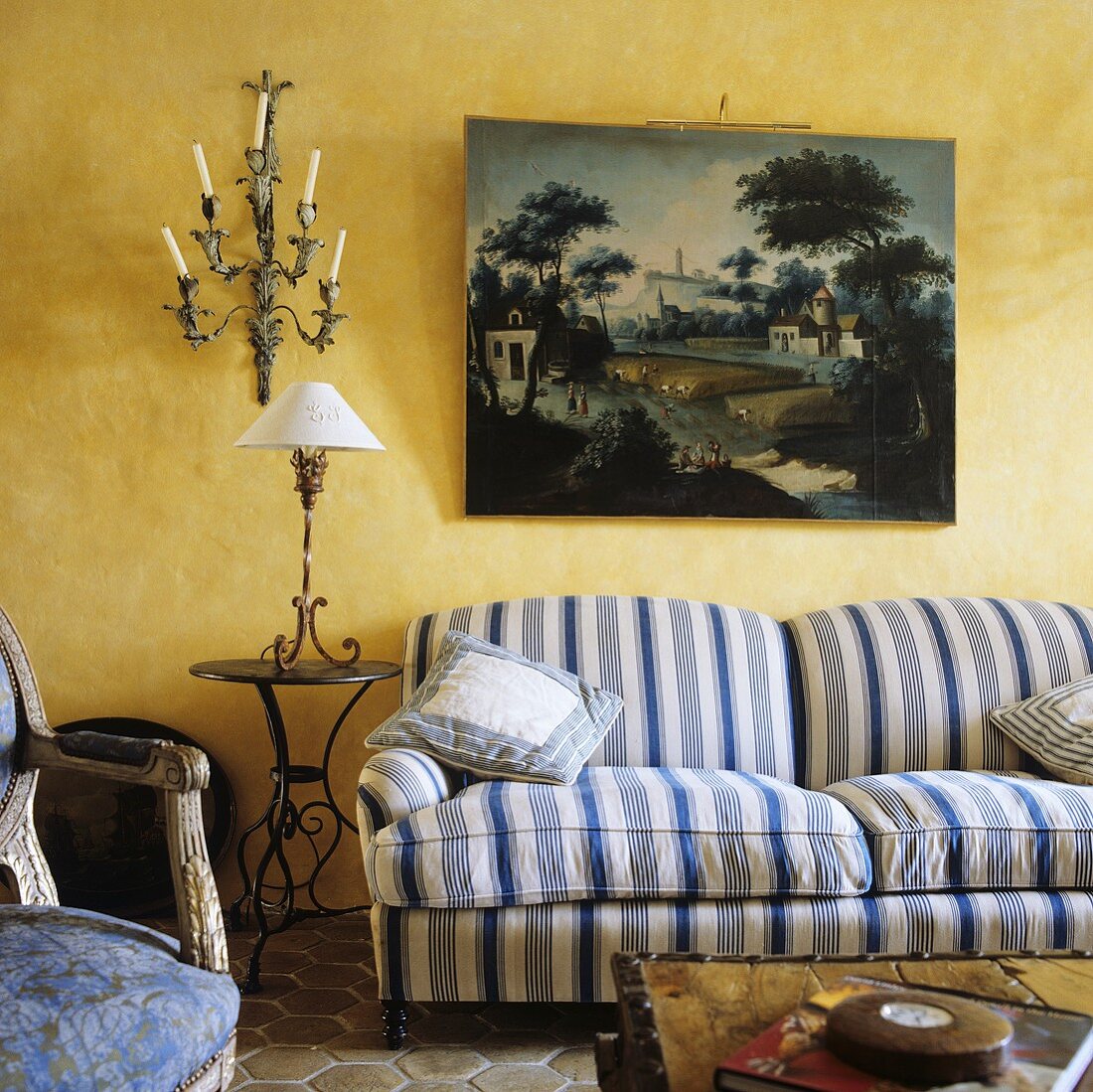 Weiß-blau gestreiftes Polstersofa unter Bild und Beistelltisch mit Tischlampe vor gelber Wand