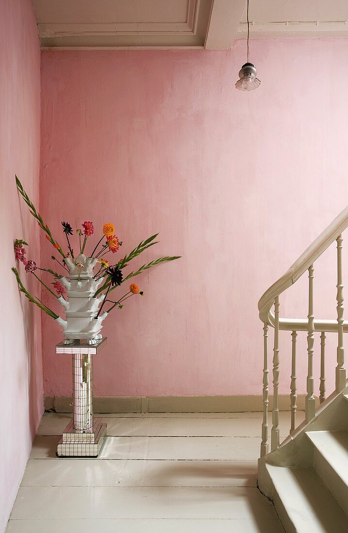A vase of flowers on a chrome pedestal against a pink wall on a landing