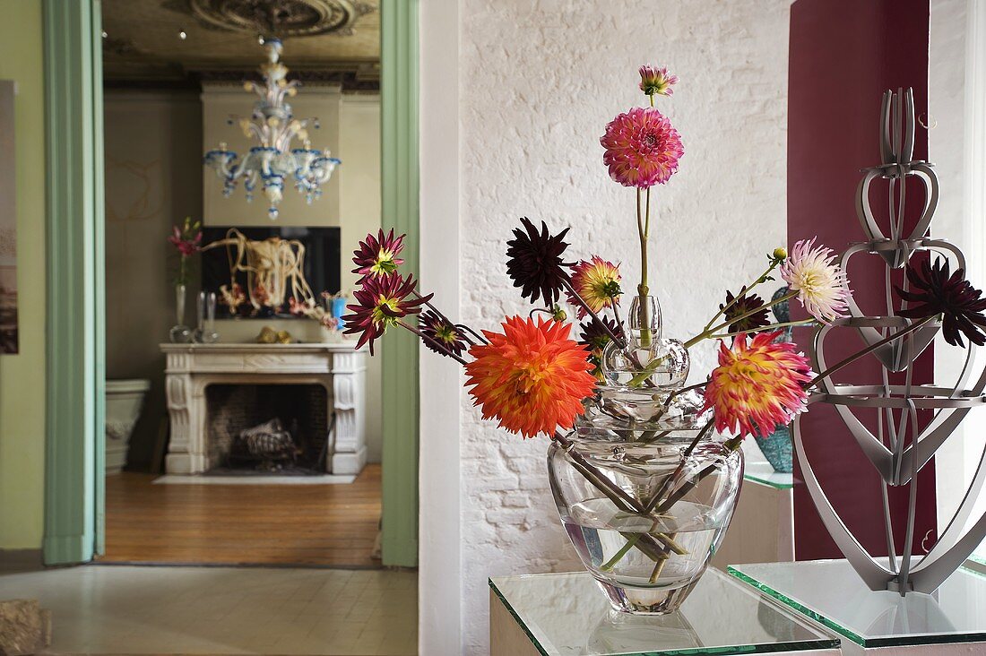 Different coloured dahlias in glass vases and a view into a living room onto the fireplace