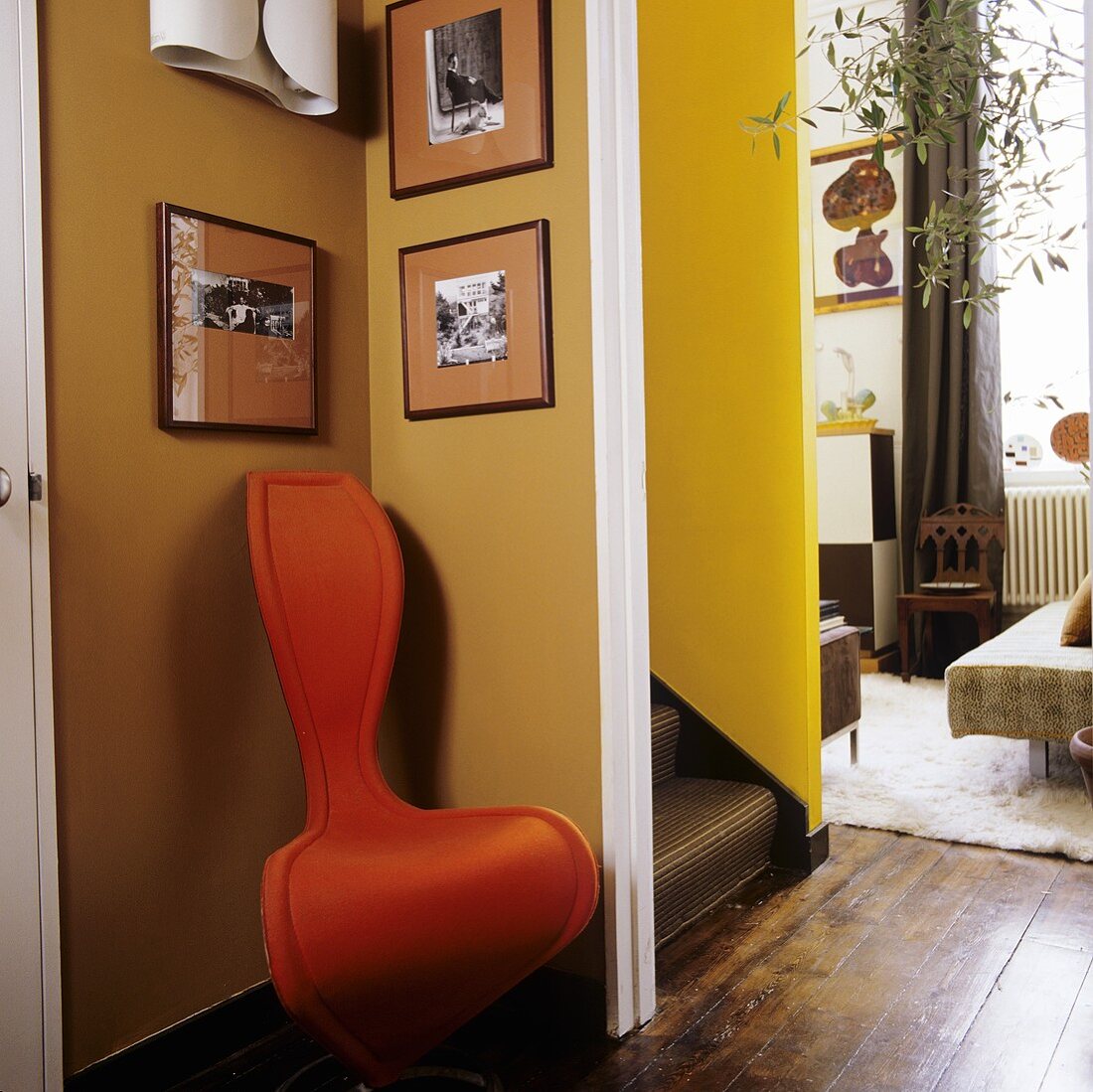 Orangefarbener Designerstuhl in der Ecke vor Treppenaufgang und Blick ins offene Wohnzimmer