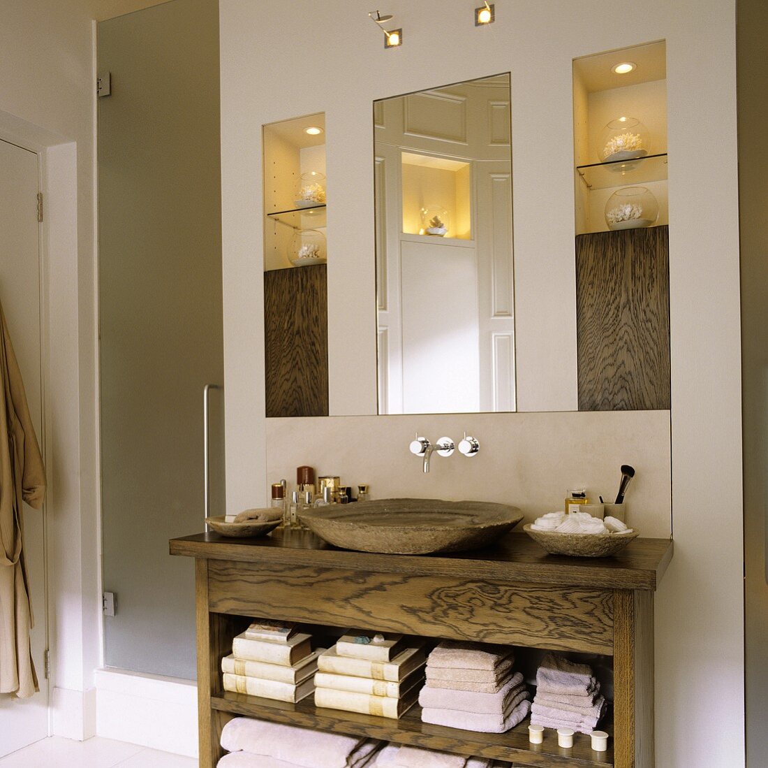 Holzwaschtisch mit rustikaler Holzschale und Spiegel neben beleuchtetem Einbauregal
