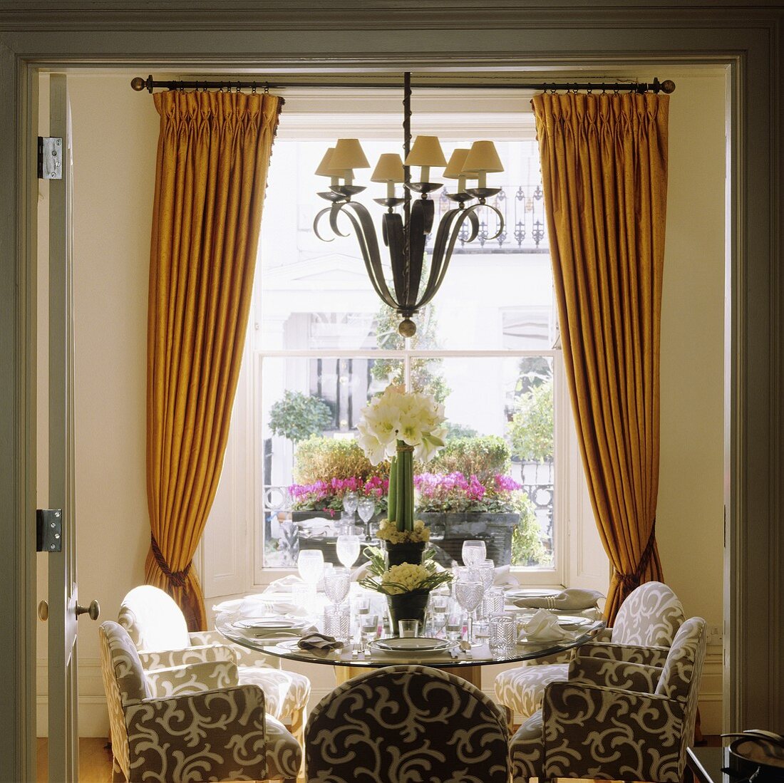 Gedeckter Esstisch vor Fenster mit gerafftem gelben Vorhang und mittig hängender Kronleuchter
