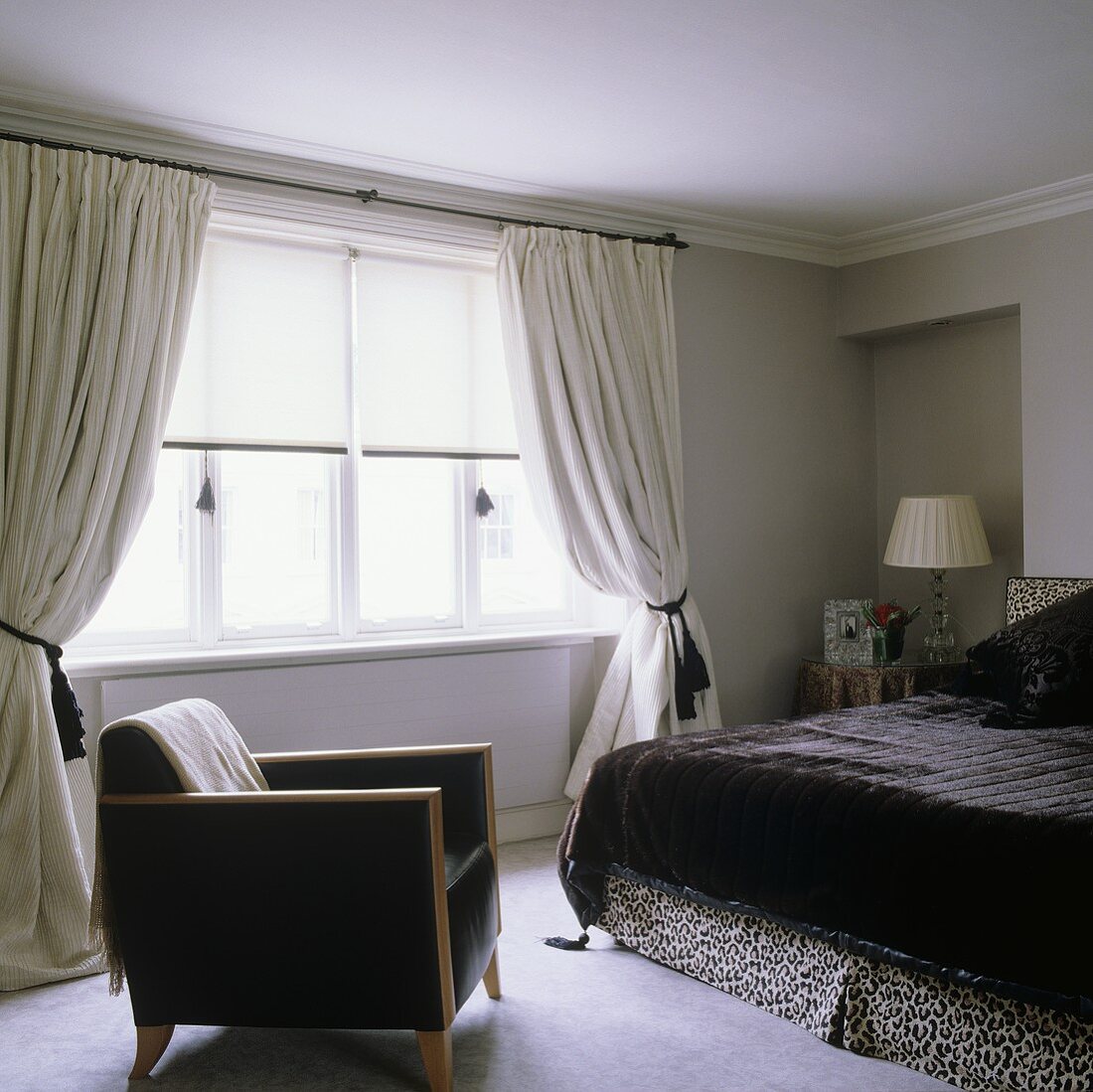 A black leather armchair and a double bed with a black fur cover in front of a window with gathered curtains