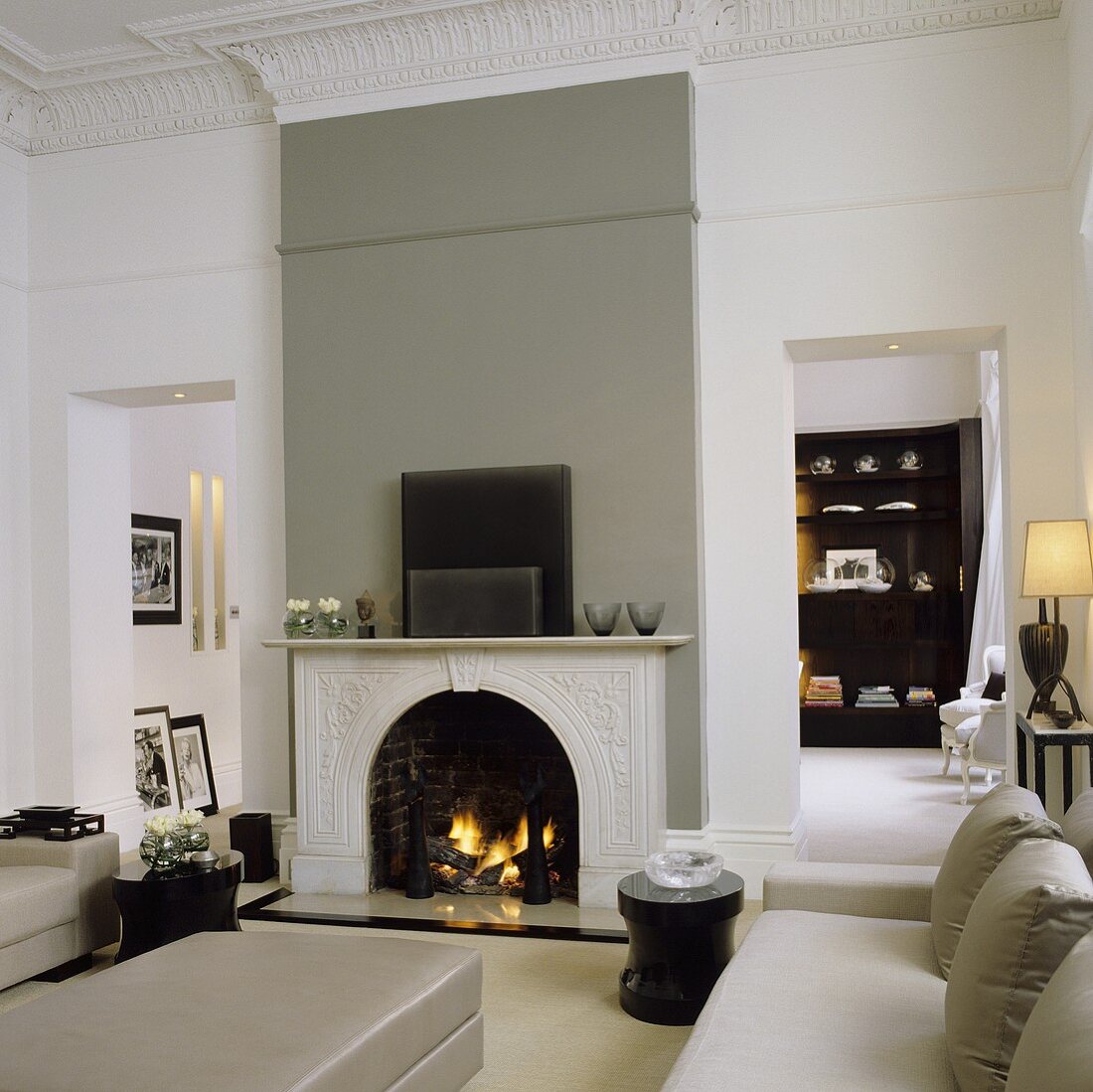 A renovated art nouveau-style living room with a grey leather sofa in front of a fireplace in a grey wall and a view of a cupboard
