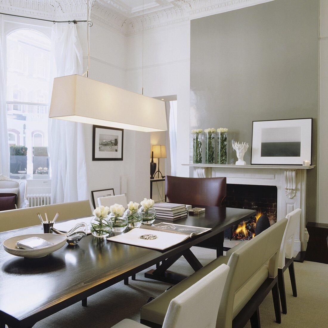An Art Deco dining area with a pendant lamp with a white shade in front of a grey-painted wall with a fireplace