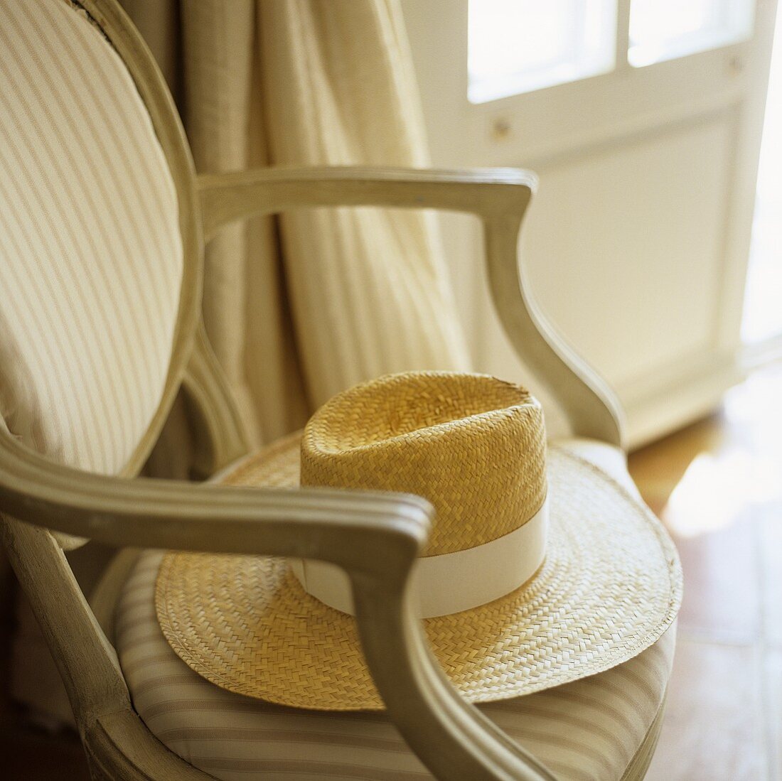 A straw hat with a white ribbon on an upholstered chair with a stripy cover