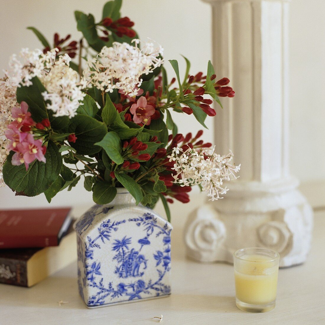 A bunch of flowers in a blue and white porcelain vase and a candle at the foot of a pillar