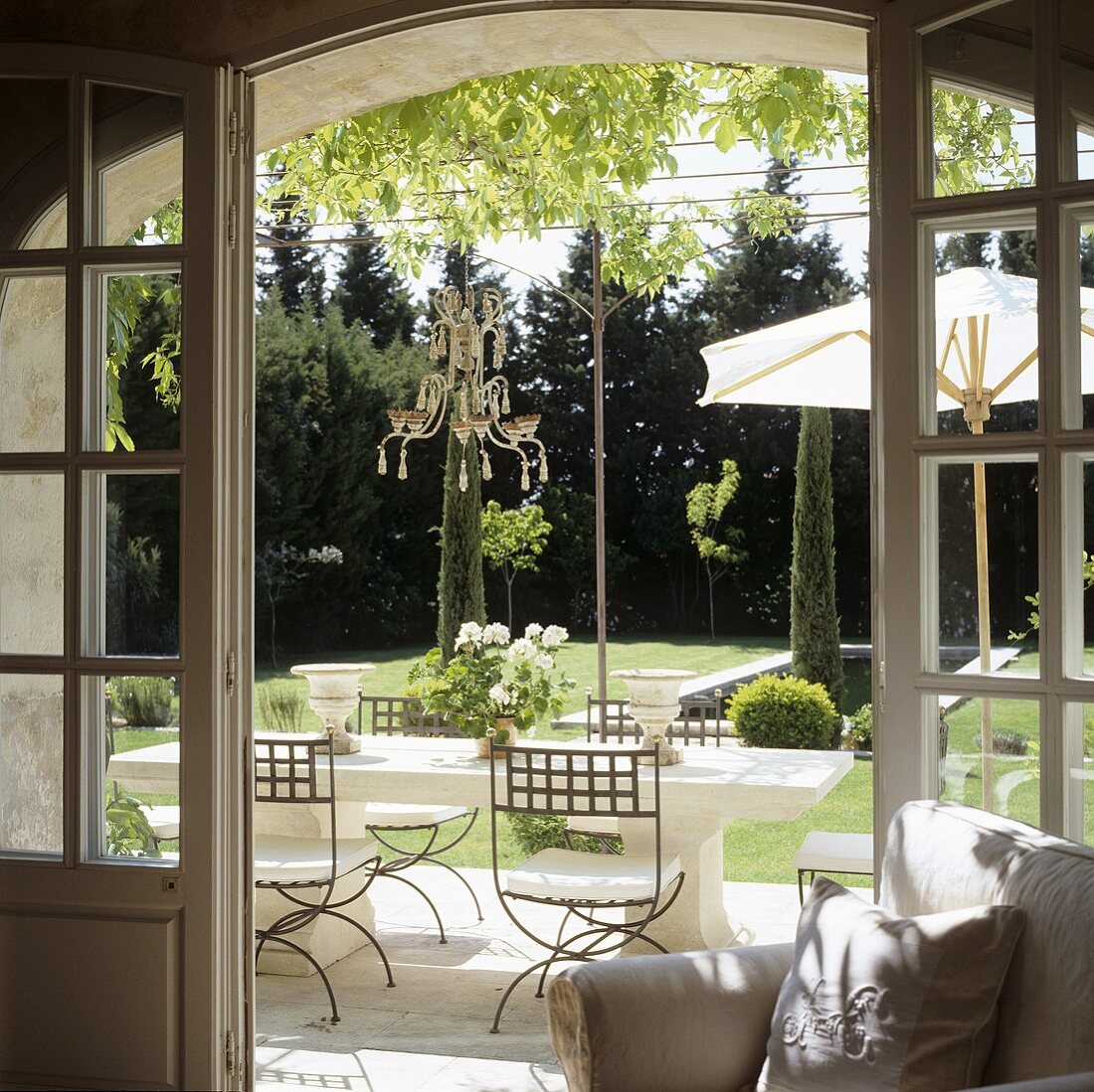 A view through an open terrace door onto elegant outdoor furniture and a Mediterranean garden