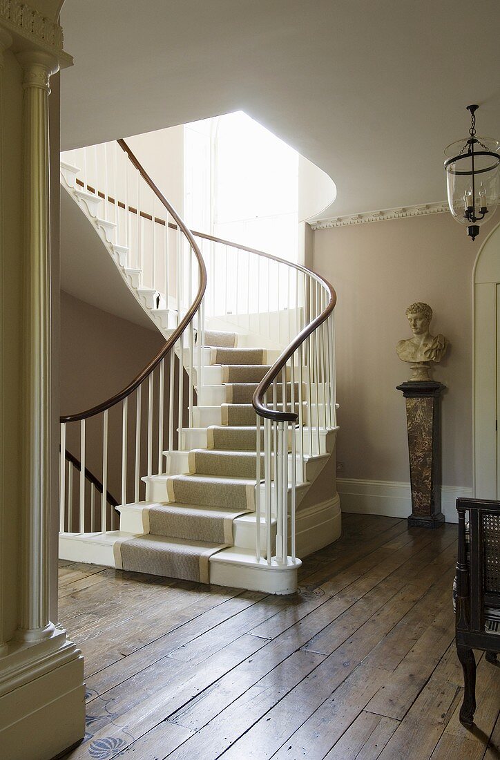 Curved staircase with carpet runner and busts on a pedestal in a stairway