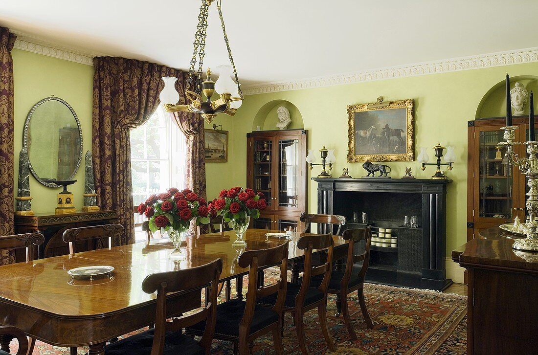An elegant dining room with green wall and a long wooden table in front of a fireplace