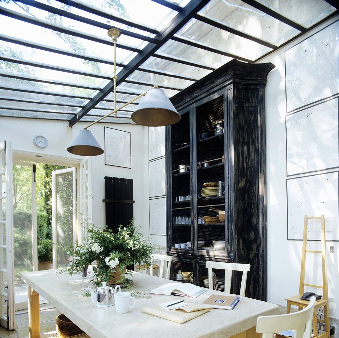 A dining room and a high black crockery cupboard in a glass extension with a door into the garden