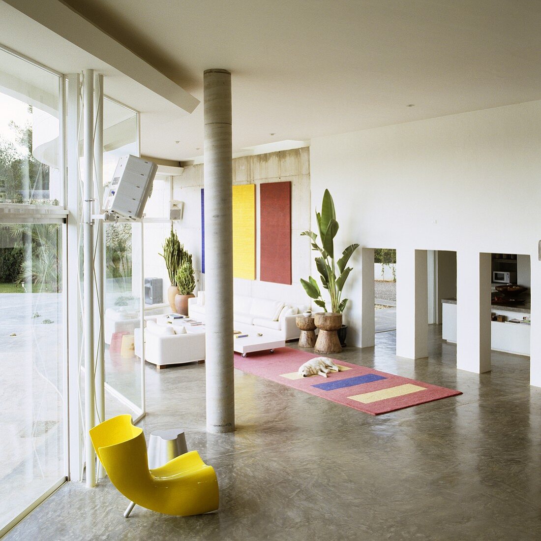 Mediterraner Haus - gelber Kunststoff Sessel vor Betonstütze und Blick auf Arkadendurchgang im offenen Wohnraum