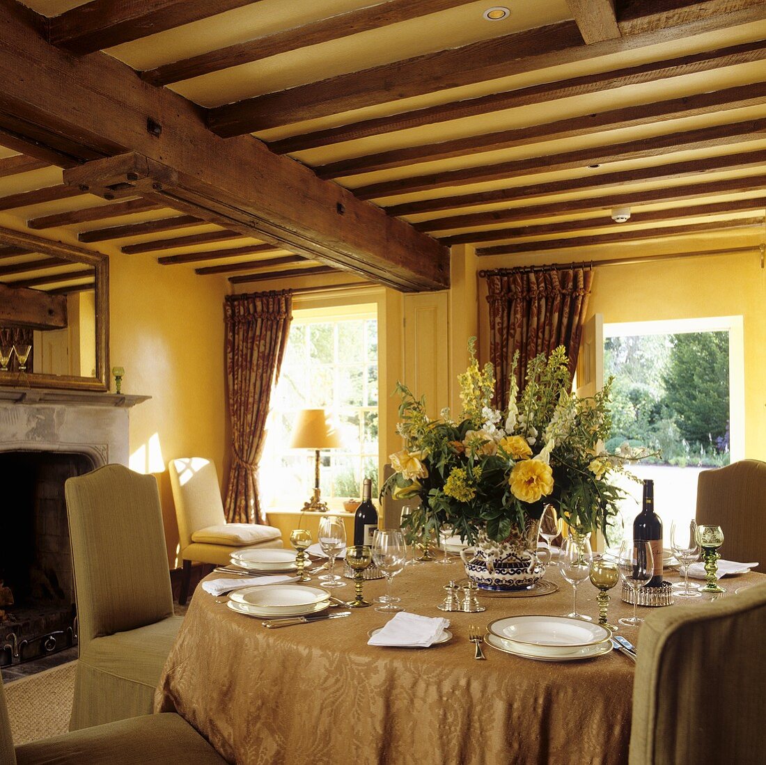 A table laid in a room with a wood beam ceiling in a yellow-painted living room in a country house