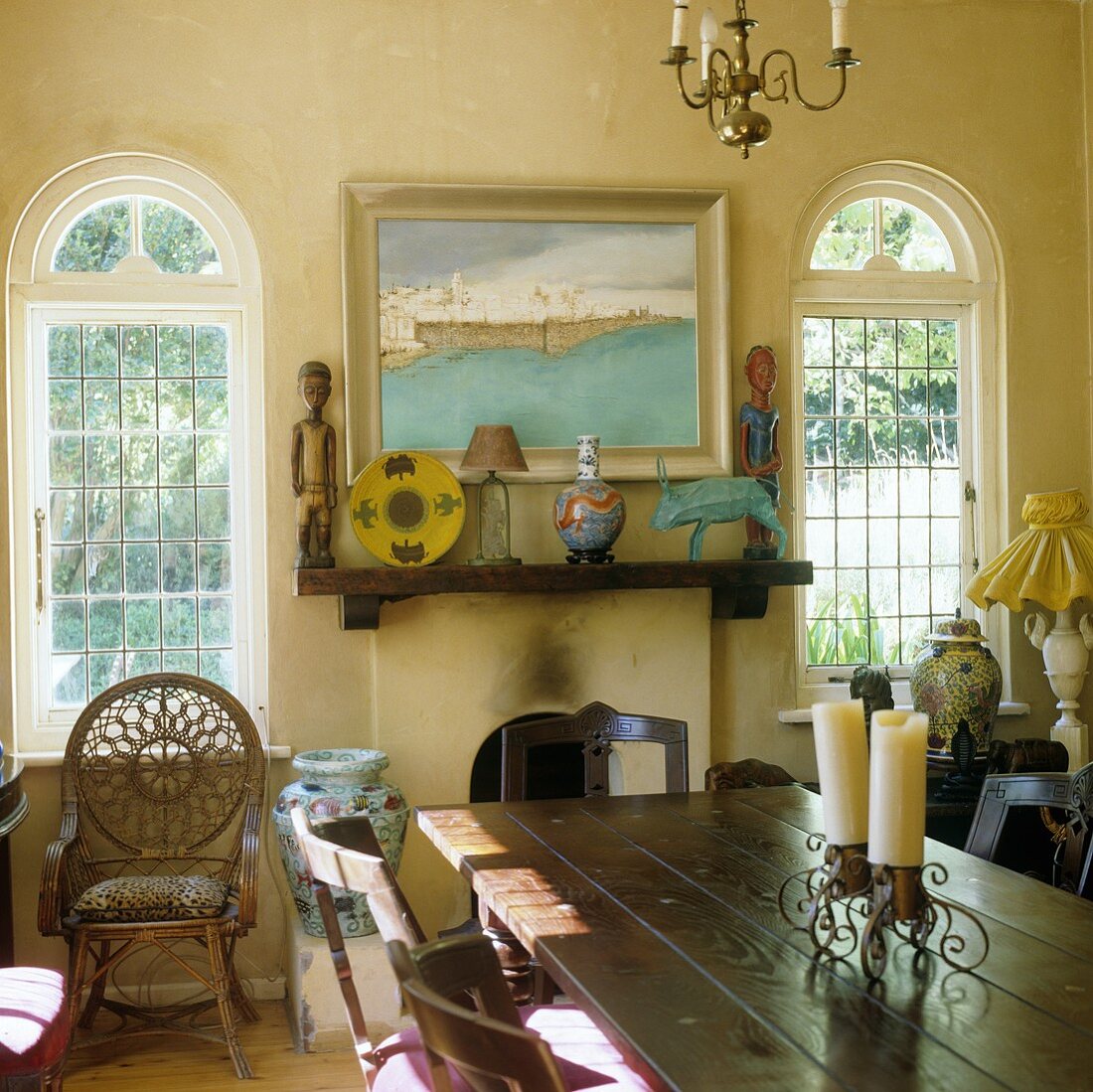 Esstisch vor Kamin mit afrikanischen Kunstobjekten und Fenster mit Rundbogen im ländlichen Wohnraum