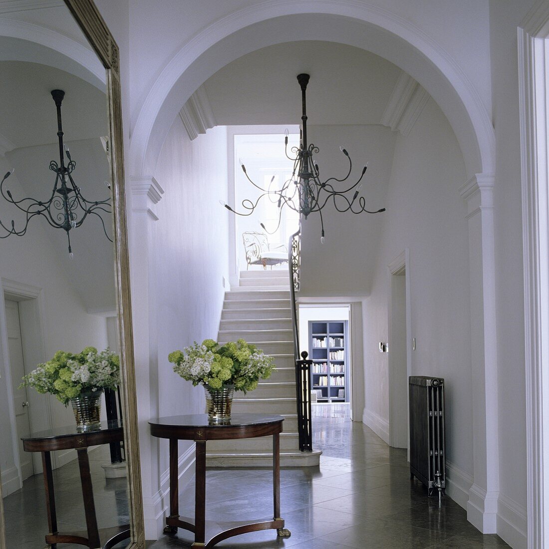 An arched doorway in an elegant hallway with a view of a stairway, an antique side table and a chandelier with Medusa-like arms