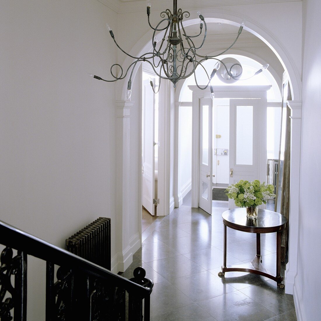 Kerzenleuchter mit Medusaarmen im eleganten Treppenhaus mit Rundbogen und Blick auf antikem Beistelltisch im Hauseingang