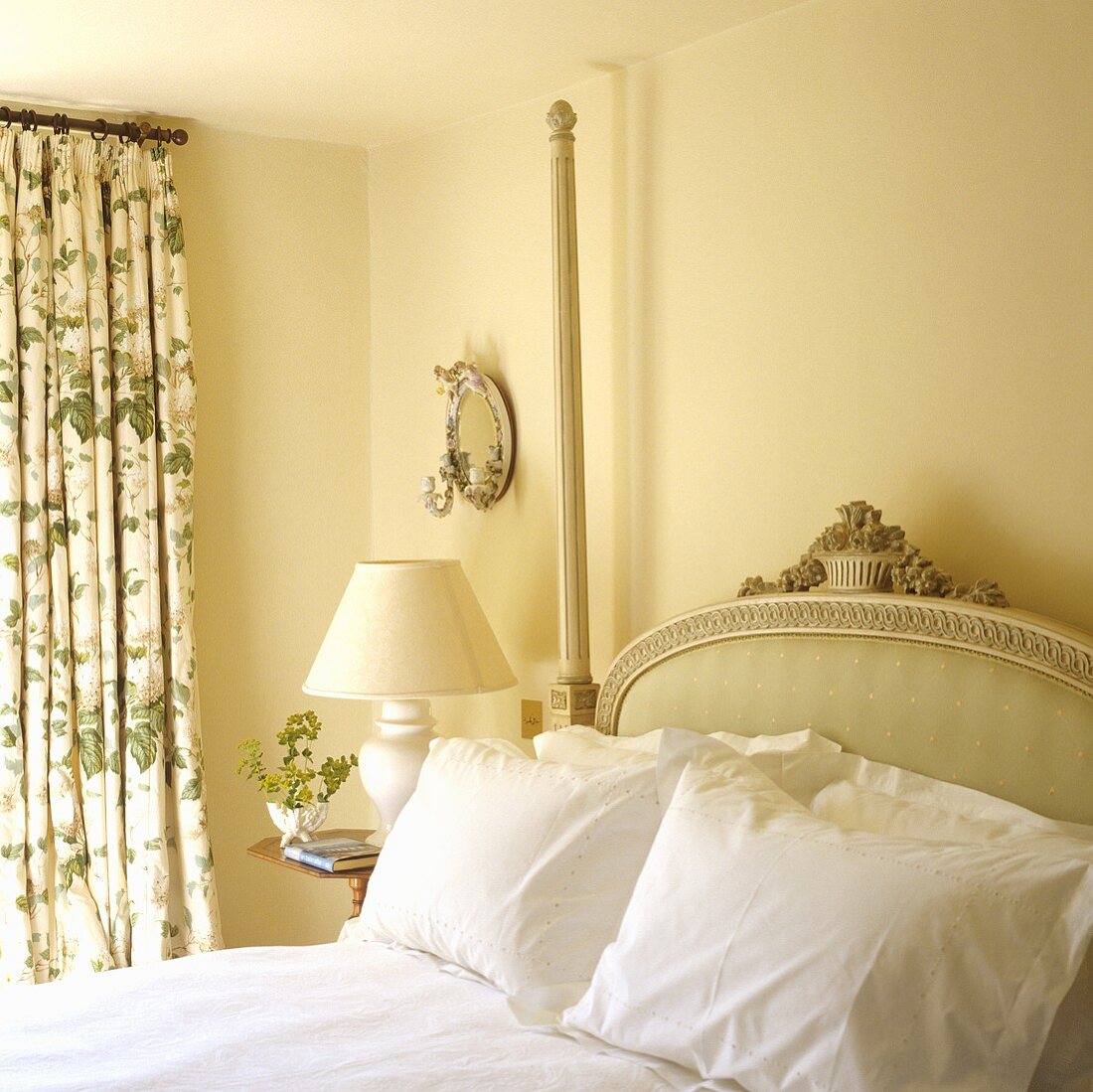 An antique bed with a padded headboard in a yellow-painted bedroom