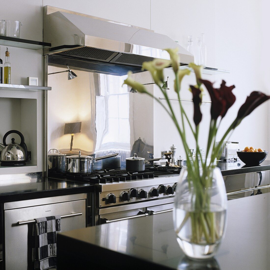 A stainless steel cooker with an extractor fan and a vase of lilies