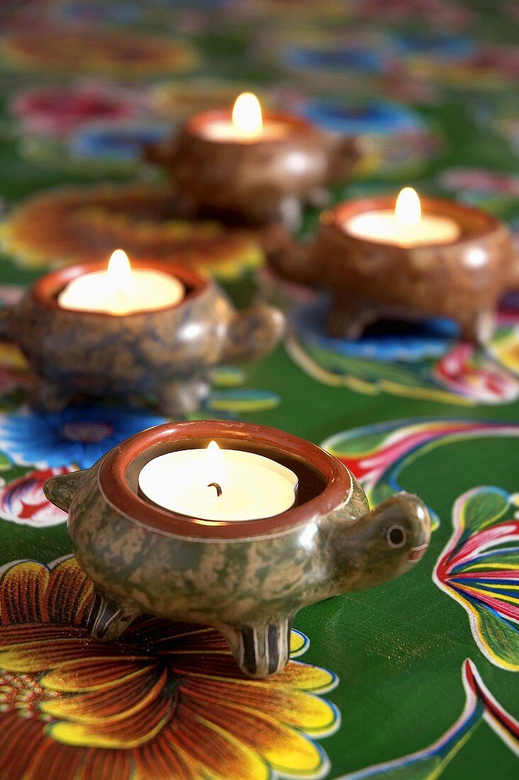Burning tea lights in holders on a colourful tablecloth