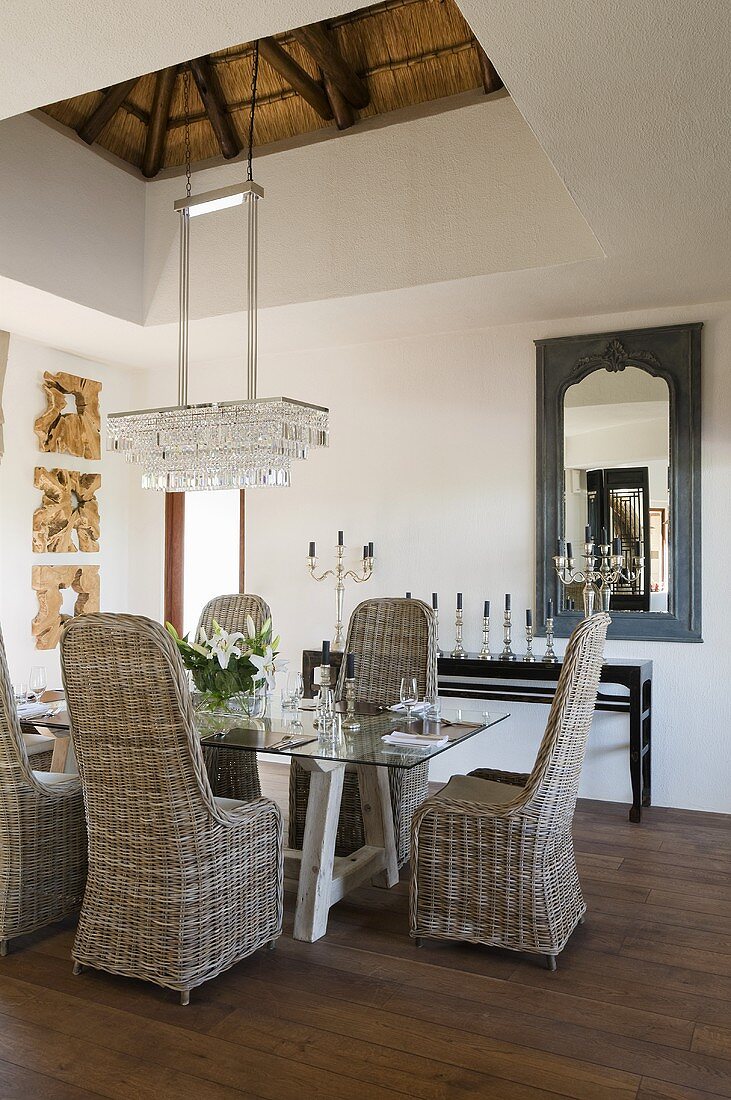 Wicker chairs around a laid table with a crystal chandelier hanging above it