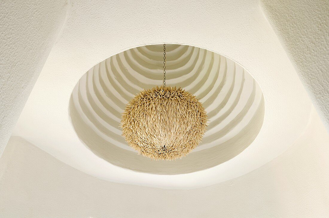 A pendent lamp with a white scraggy shade in a ceiling niche