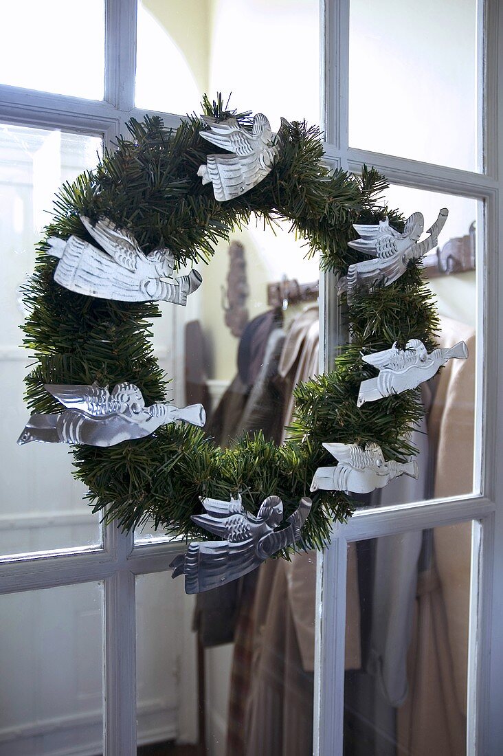 Adventskranz mit silbernen Engeln an verglaster Tür vor Garderobe
