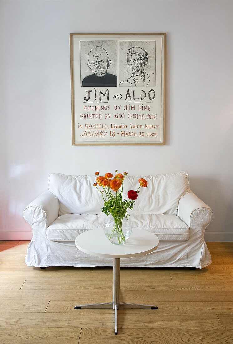 Flowers on a bistro table with metal base in front of a white sofa and a drawing on the wall