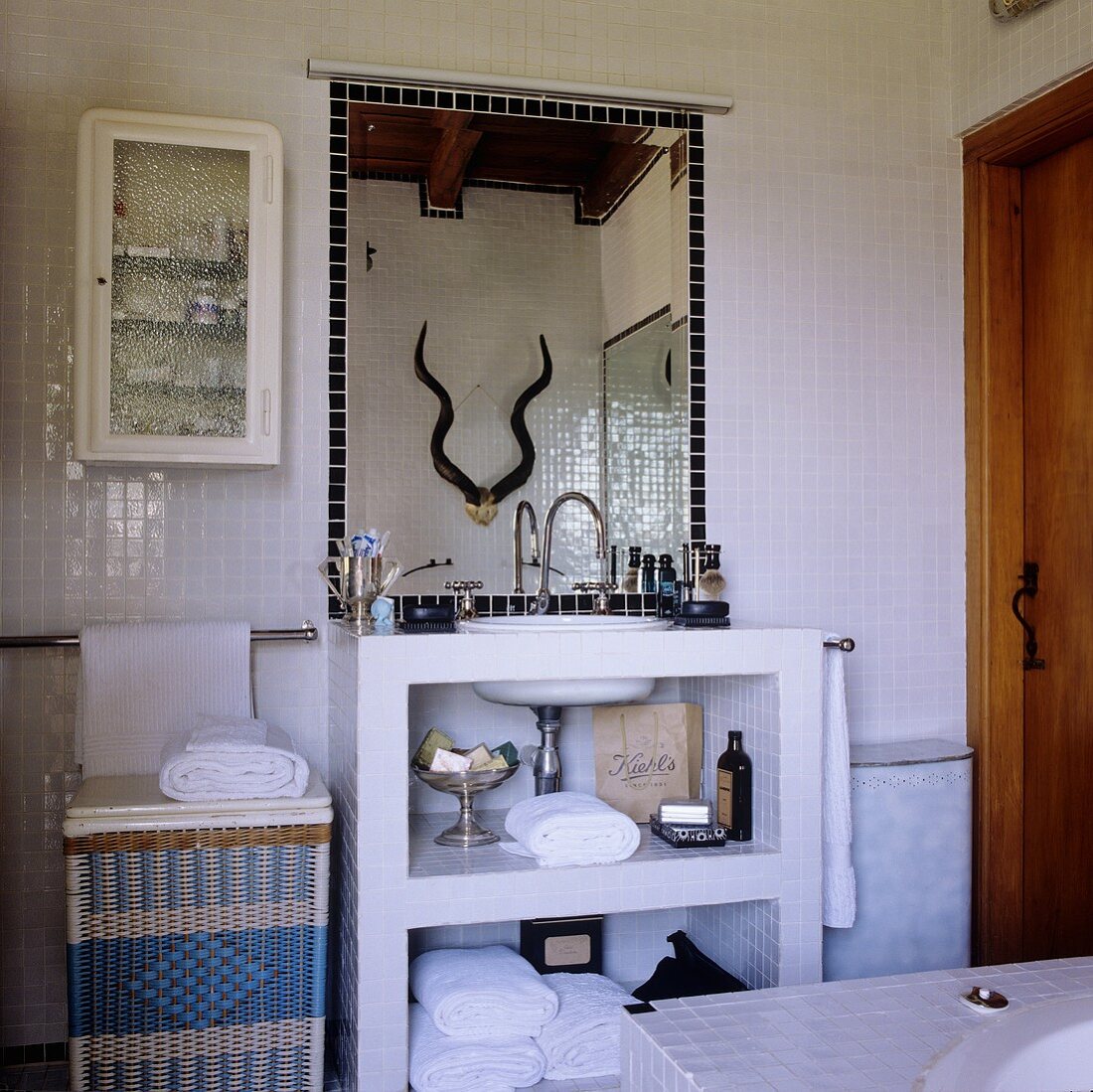 A bathroom in a South African country house - a stone wash stand with a mirror on a white, mosaic-tiled wall
