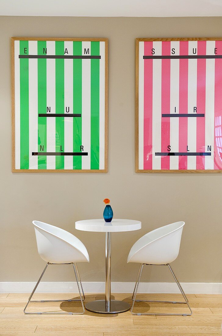 Bucket chairs and a bistro table in front of a grey wall hung with posters