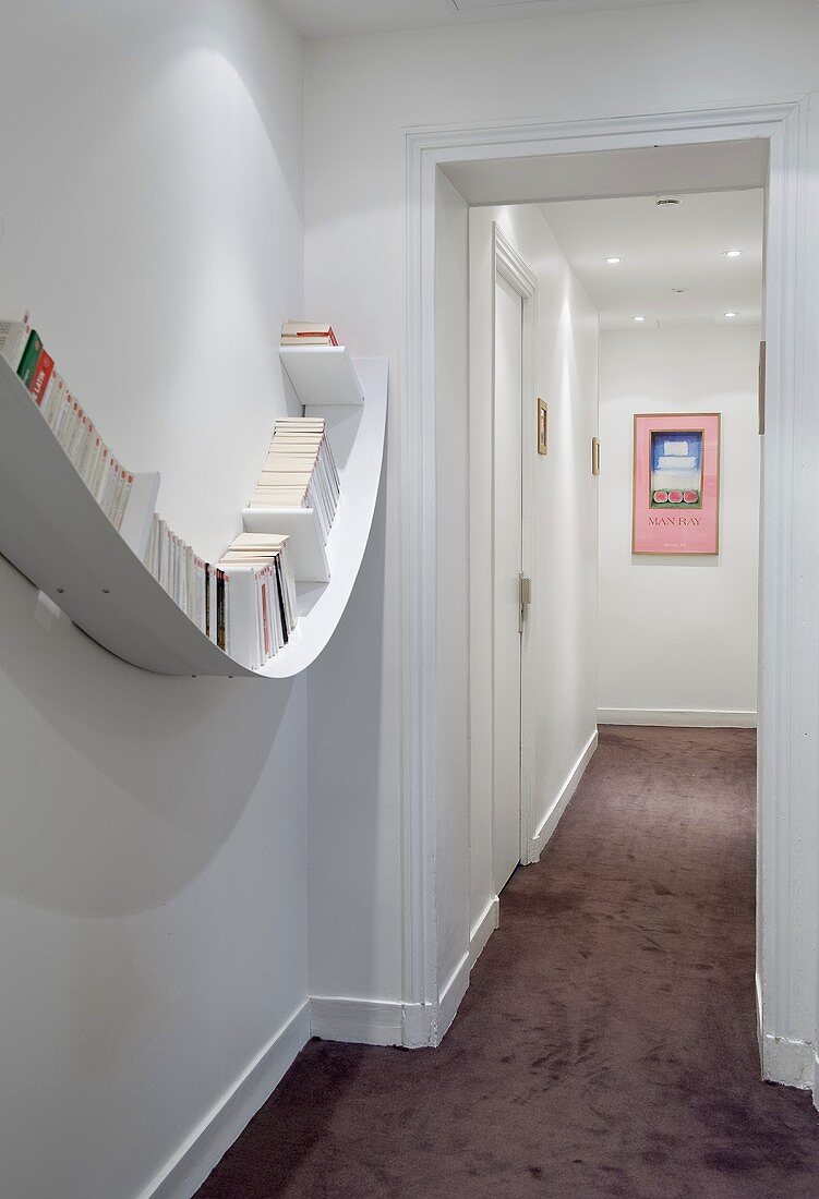 A narrow, illuminated hallway - a curved wall shelf and a blackberry-coloured carpet