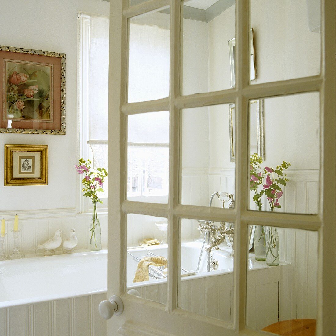 Geöffnete Badtür mit Blick auf weiße Badewanne und Bilder mit Goldrahmen an Wand
