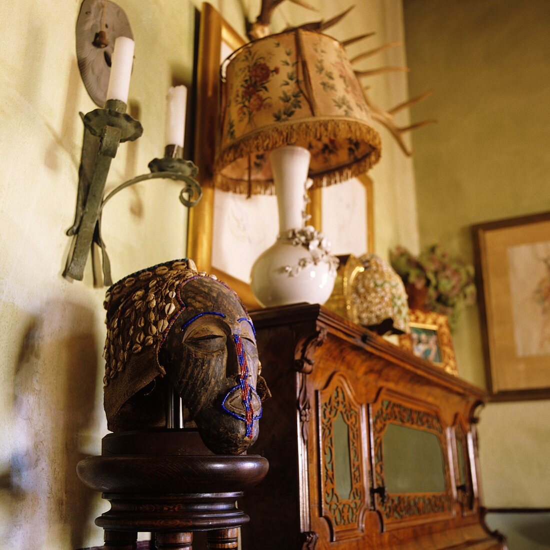 Tischlampe mit Stoffschirm auf antikem Holzschrank und bemalte Portraitskulptur aus Holz