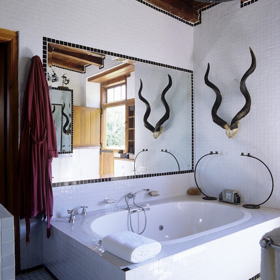 A bathroom in a South African country house with a bathtub and a mirror in front of white mosaic-tiled wall