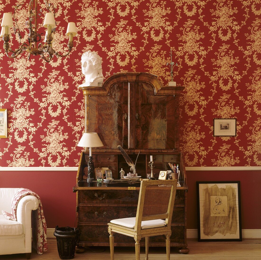 An antique wooden davenport against a wall papered with decorative red and white paper