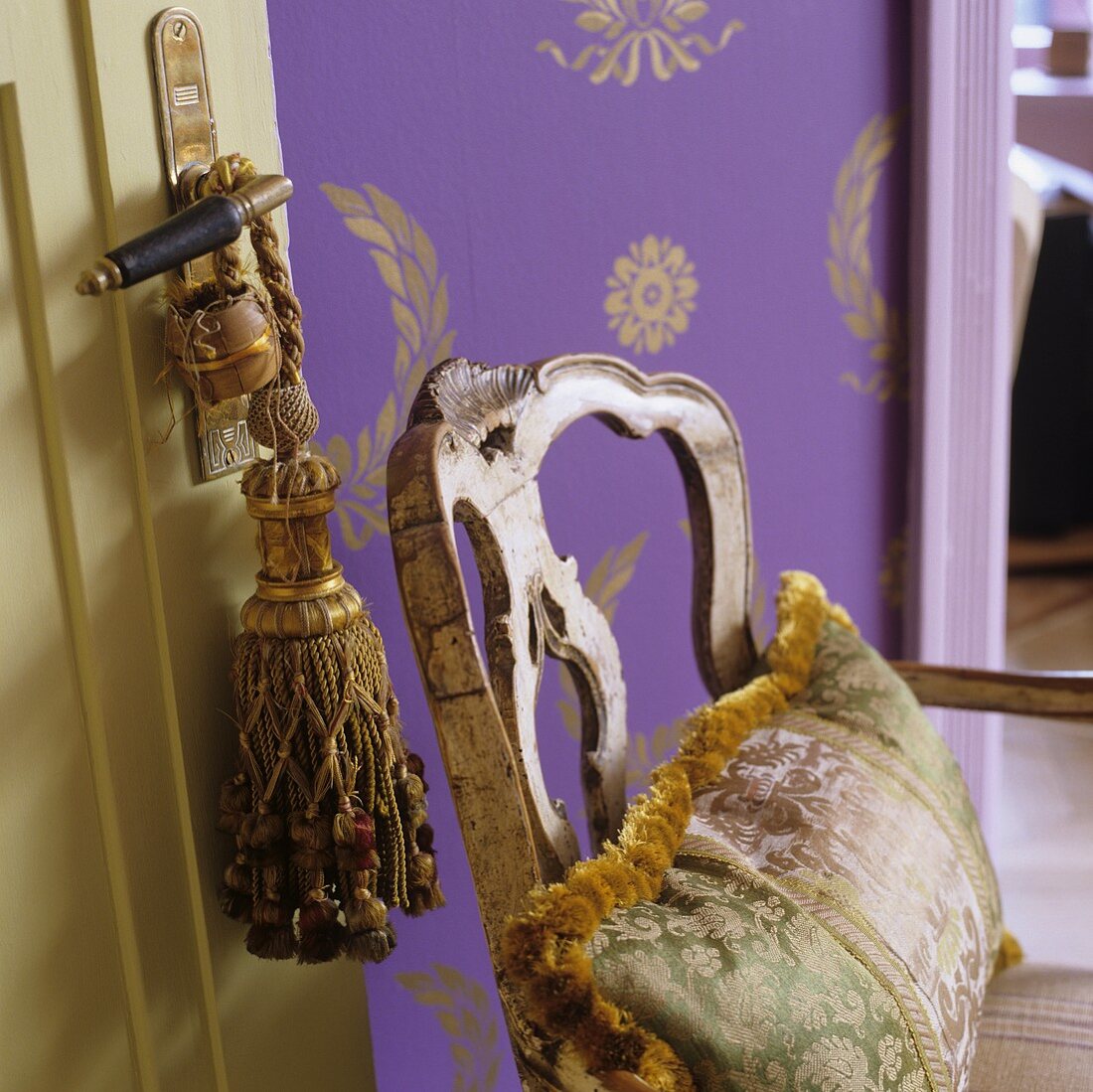 Seidenkissen auf Vintage Holzstuhl vor lila Tapete mit goldenem Ornamentmuster